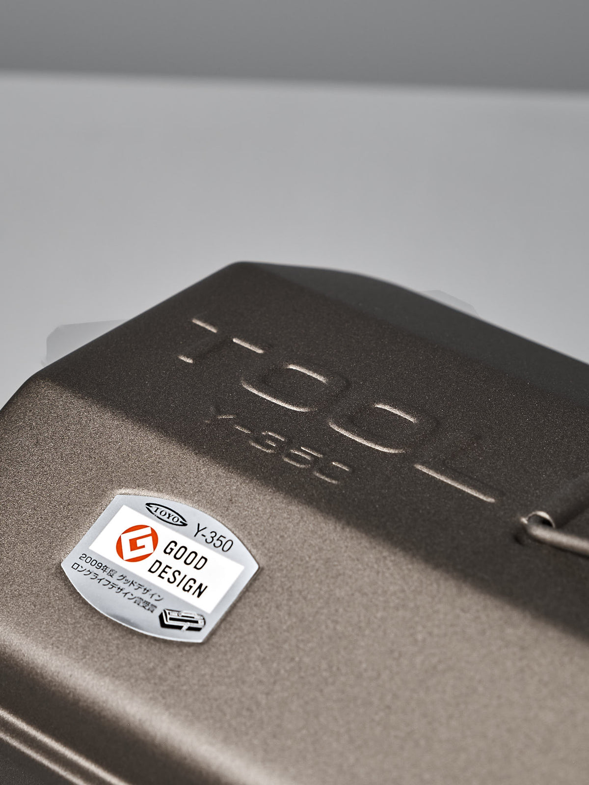 Close-up of the Camber-Top Toolbox Y-350 – Titanium by TOYO STEEL, showcasing a dark metallic surface with the "TOOL Y-350" engraving and a "Good Design Award 2009" label. Crafted from powder-coated steel, it combines durability with style.