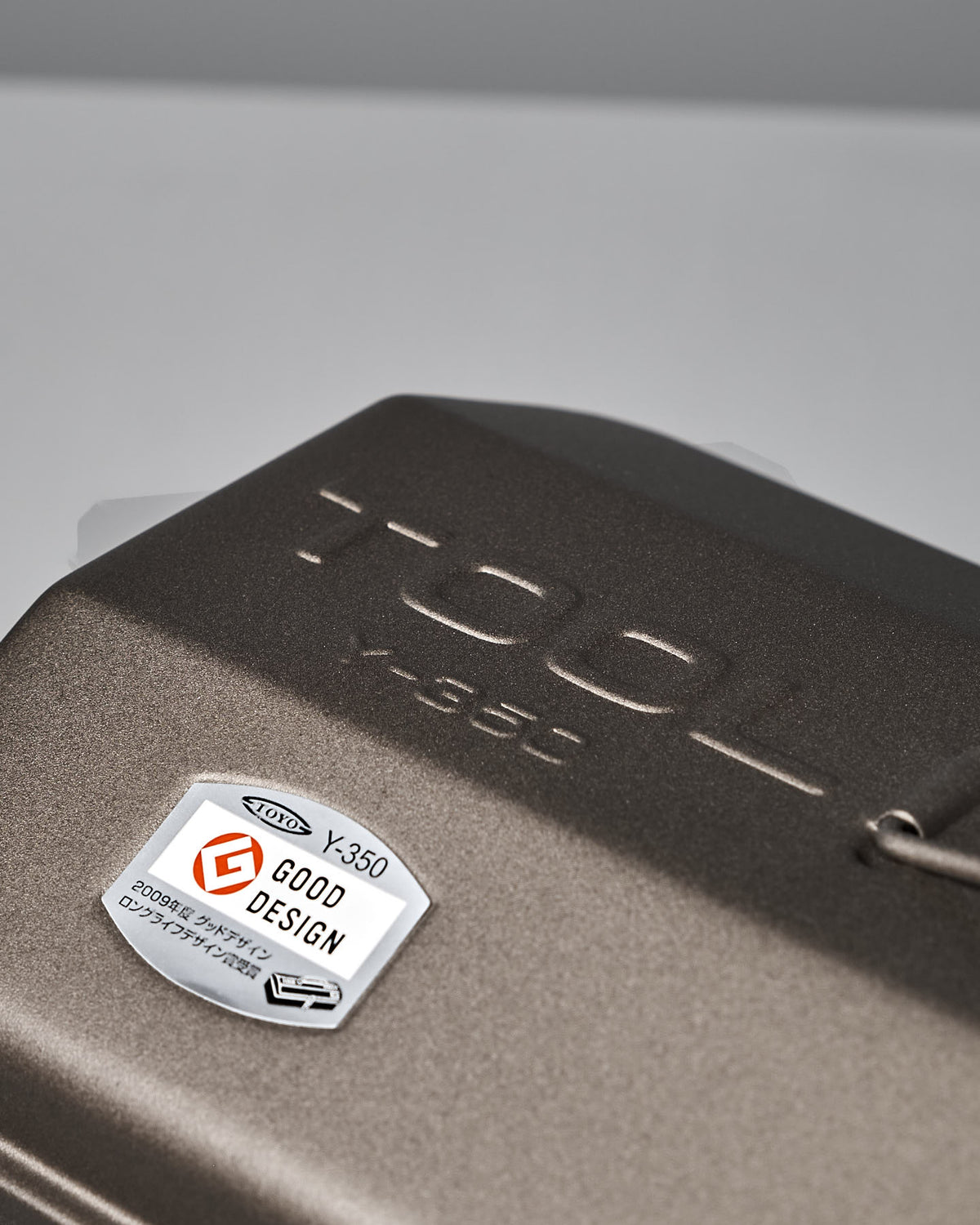 Close-up of the Camber-Top Toolbox Y-350 – Titanium by TOYO STEEL, showcasing a dark metallic surface with the "TOOL Y-350" engraving and a "Good Design Award 2009" label. Crafted from powder-coated steel, it combines durability with style.
