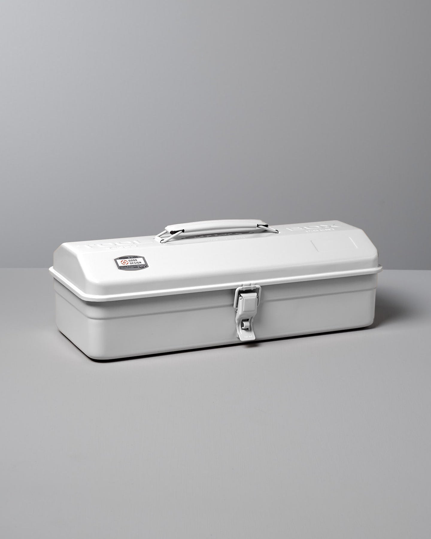 The TOYO STEEL Camber-Top Toolbox Y-350 in white, made from powder-coated steel, features a handle and latch and is displayed gracefully on a gray surface.