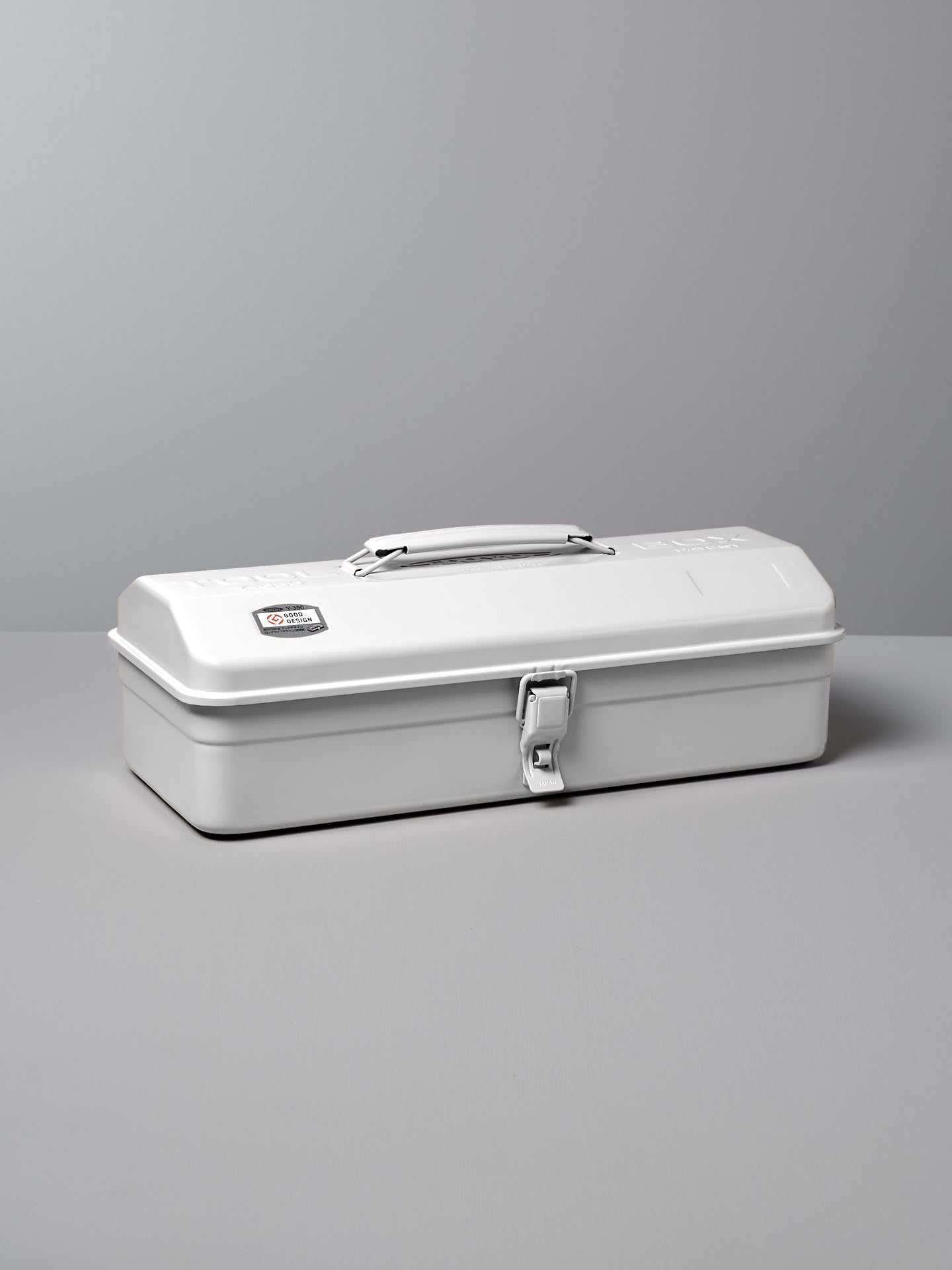 The TOYO STEEL Camber-Top Toolbox Y-350 in white, made from powder-coated steel, features a handle and latch and is displayed gracefully on a gray surface.