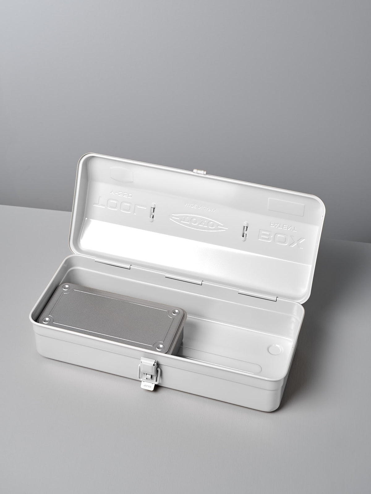 A Camber-Top Toolbox Y-350 in white by TOYO STEEL, made from powder-coated steel, sits on a gray surface with its lid open. Inside, you&#39;ll discover a sleek rectangular metal object and a well-designed compartment reflecting its Good Design Award heritage.