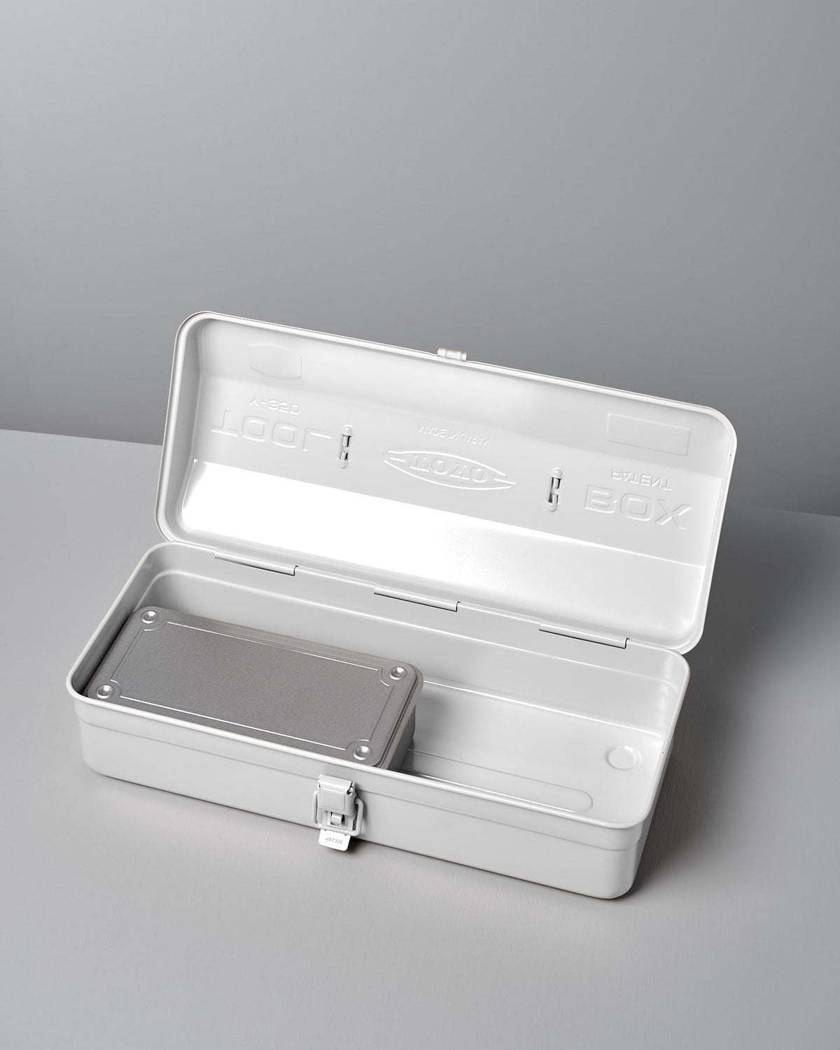 A Camber-Top Toolbox Y-350 in white by TOYO STEEL, made from powder-coated steel, sits on a gray surface with its lid open. Inside, you'll discover a sleek rectangular metal object and a well-designed compartment reflecting its Good Design Award heritage.