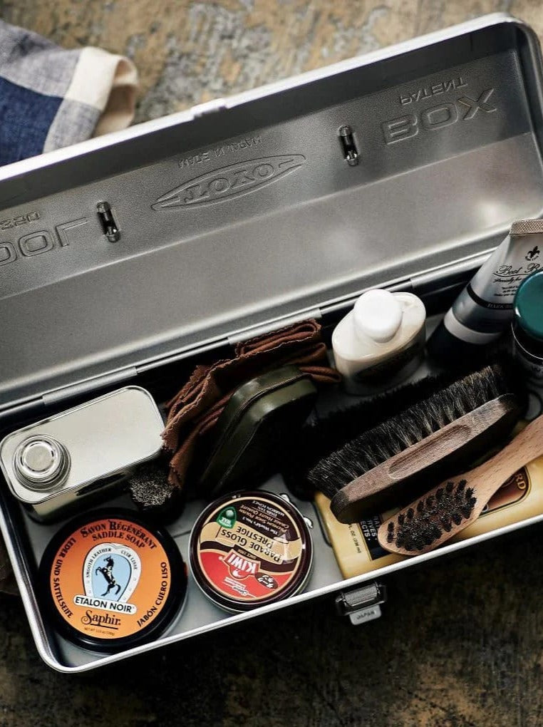 An open TOYO STEEL Camber-Top Toolbox Y-350 – Beige with various shoe polishing supplies, including brushes, polishes, a cloth, and a small can. Crafted in Osaka, Japan, this kit exudes quality and functionality. Its elegant design even earned a Good Design Award for its impeccable form and utility.