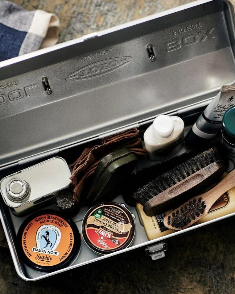 An open TOYO STEEL Camber-Top Toolbox Y-350 – Beige with various shoe polishing supplies, including brushes, polishes, a cloth, and a small can. Crafted in Osaka, Japan, this kit exudes quality and functionality. Its elegant design even earned a Good Design Award for its impeccable form and utility.