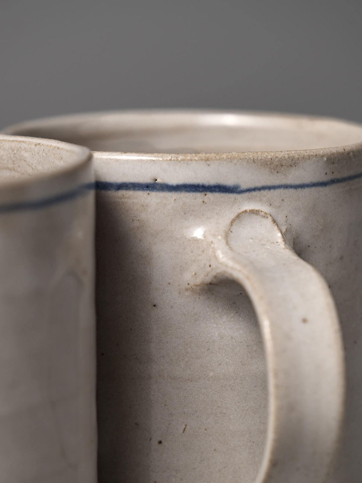 Close-up of two Zoë Isaacs Coffee Cup – Cobalt Line pieces, featuring hand-painted matte blue-grey glaze, curved handles, and a thin cobalt rim—showcasing the uniqueness of handmade design.