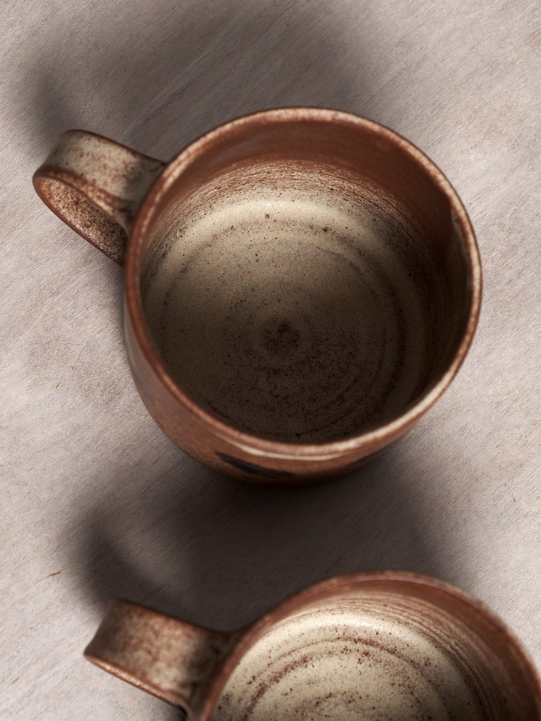 Two handmade brown Spots mugs with a matte cream glaze on a wooden surface.