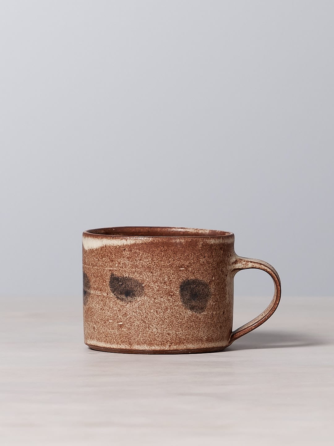 A small brown Spots mug with a matte cream glaze sitting on a wooden table.