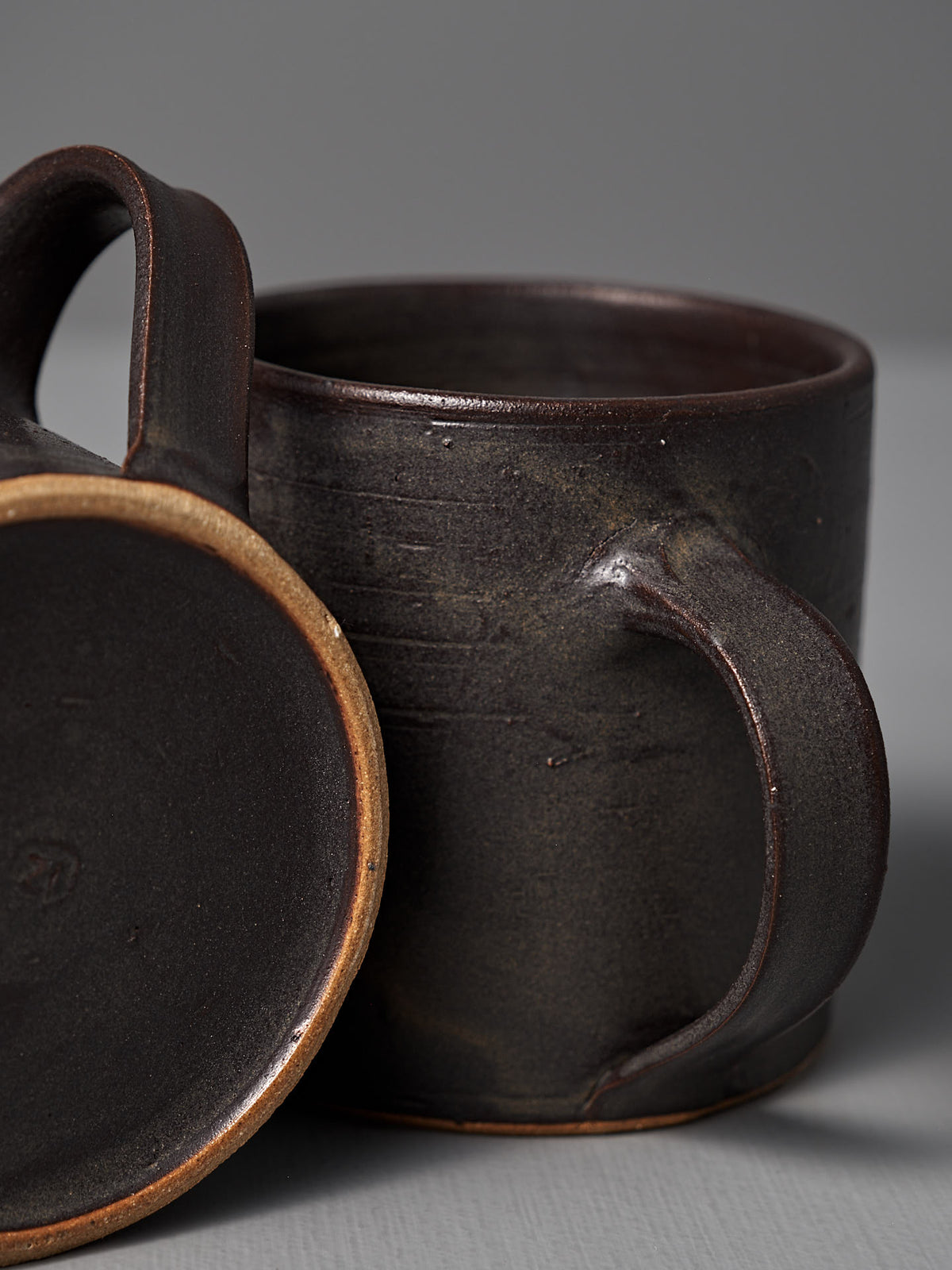 Two Zoë Isaacs Coffee Cup – Dapple Brown mugs are shown—one standing upright and the other on its side—against a plain gray background.