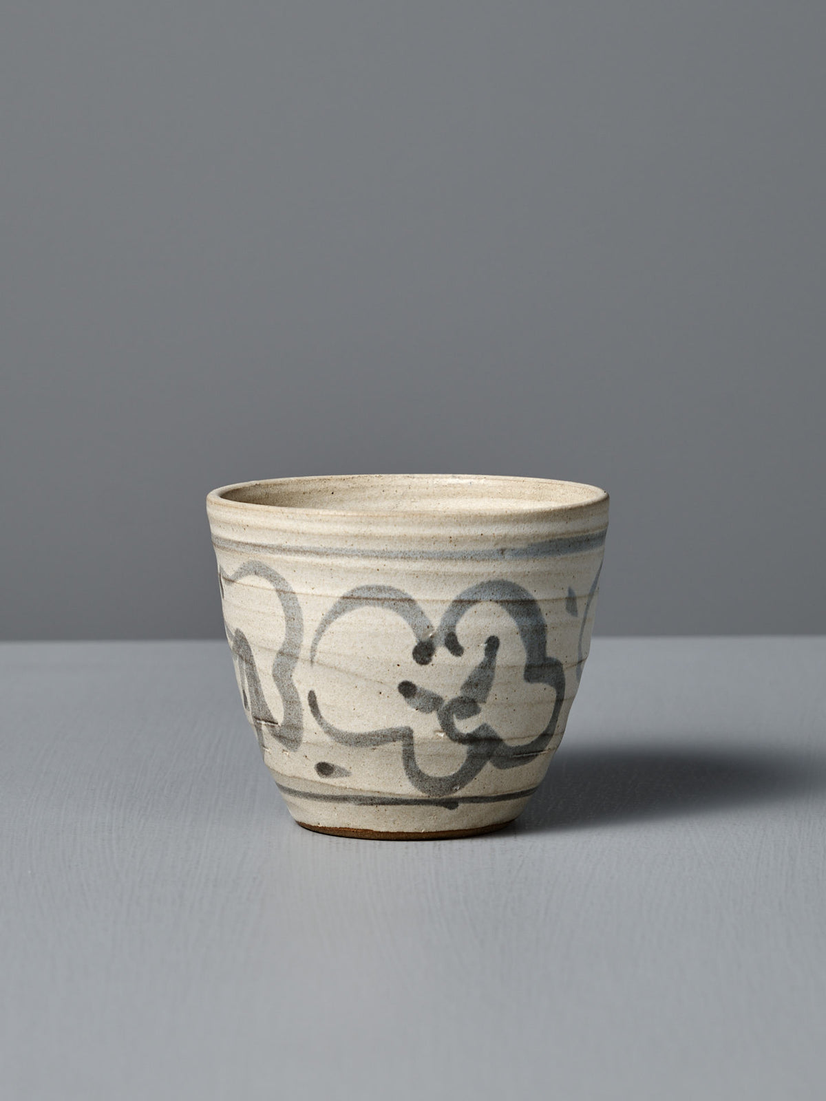The Cup – Floral, a handmade ceramic cup featuring a light gray glaze and abstract black brushstroke design, is displayed on a flat surface against a plain gray background.