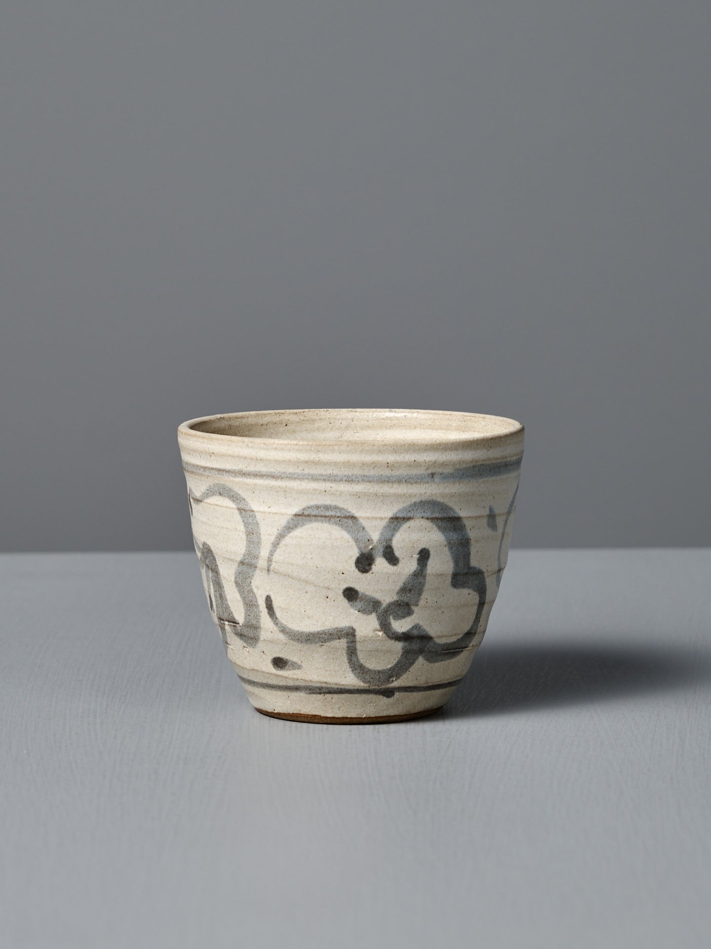 The Cup – Floral, a handmade ceramic cup featuring a light gray glaze and abstract black brushstroke design, is displayed on a flat surface against a plain gray background.
