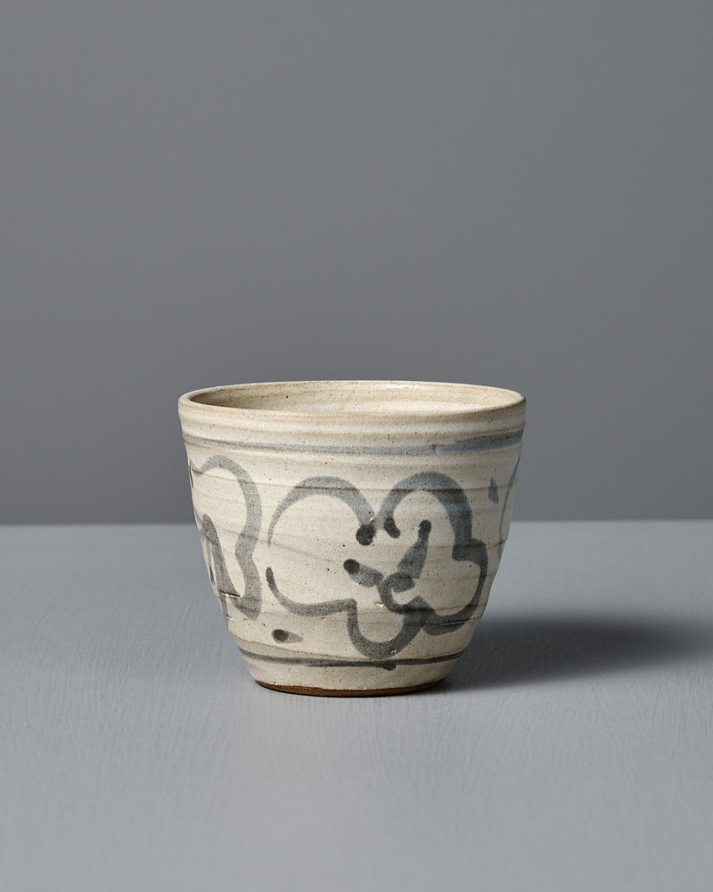 The Cup – Floral, a handmade ceramic cup featuring a light gray glaze and abstract black brushstroke design, is displayed on a flat surface against a plain gray background.