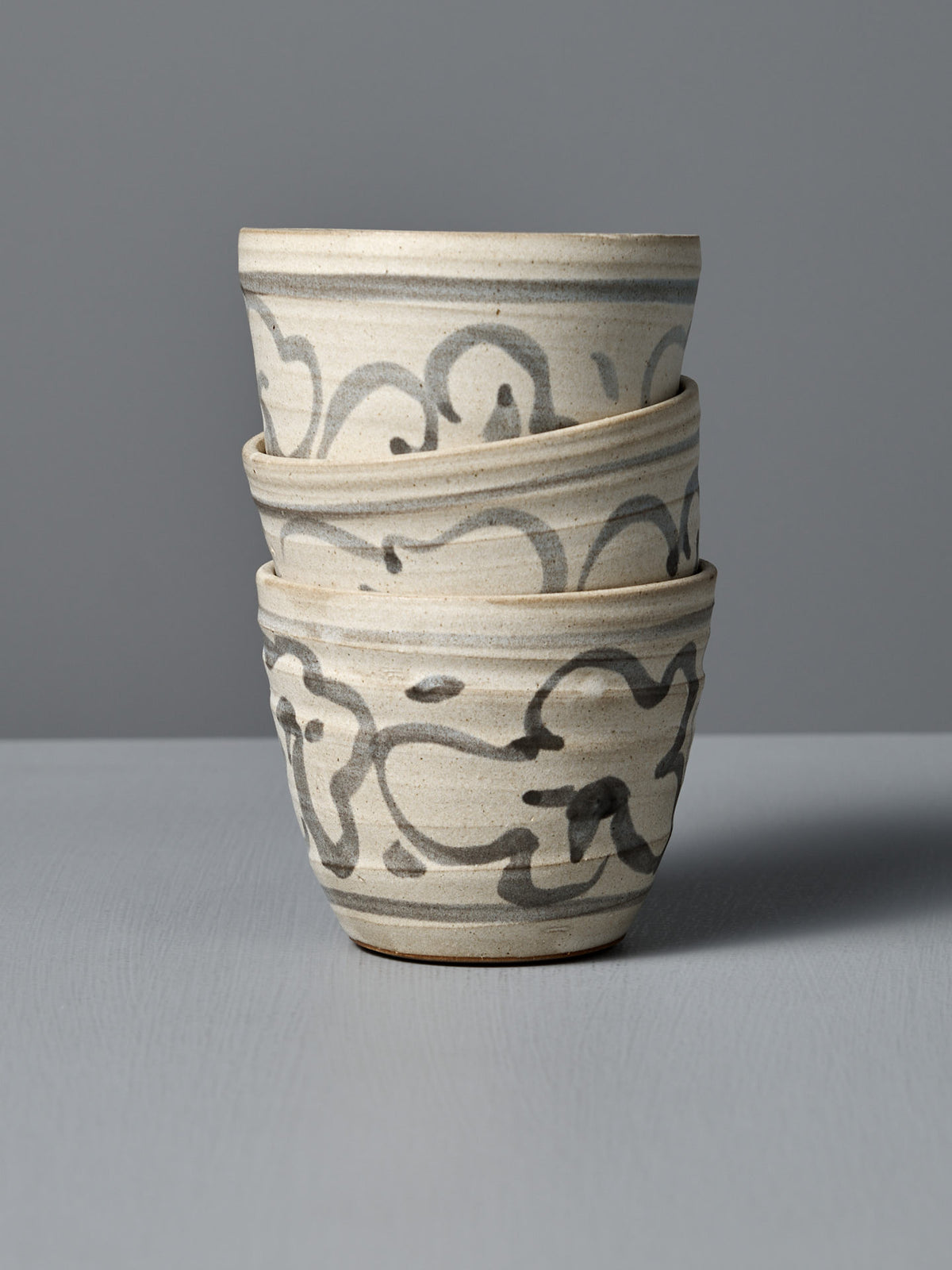 A handmade ceramic cup titled "Cup – Floral," featuring a grayish-white glaze and abstract black patterns, crafted in Aotearoa and photographed against a plain gray background.