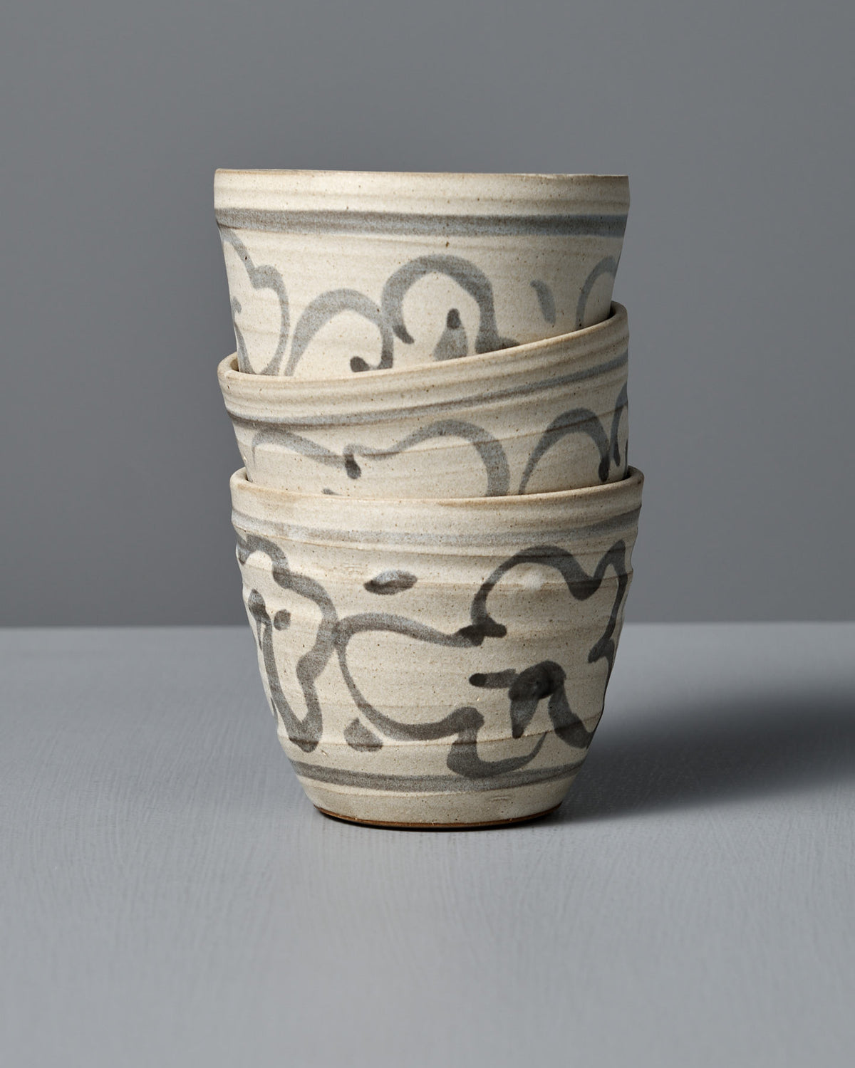 A handmade ceramic cup titled "Cup – Floral," featuring a grayish-white glaze and abstract black patterns, crafted in Aotearoa and photographed against a plain gray background.