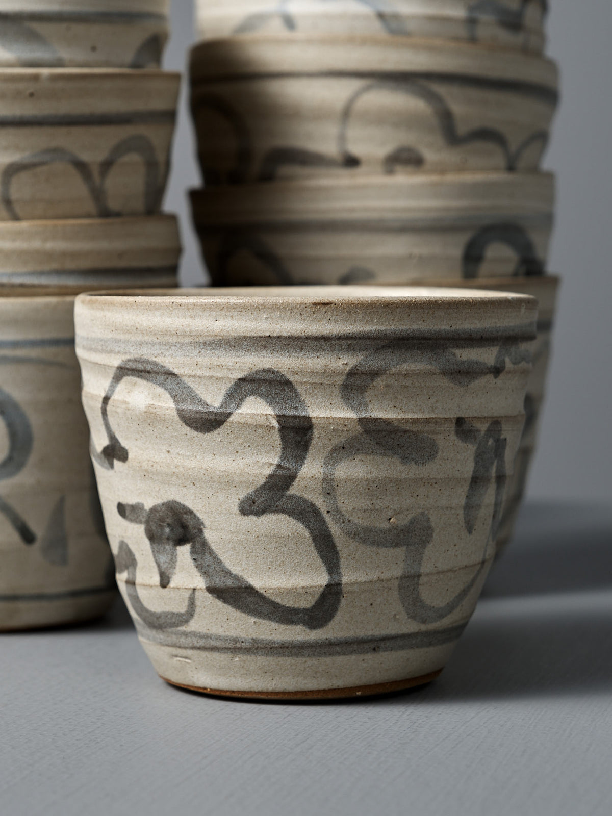 A Cup – Floral with a matte cream glaze and black abstract floral patterns is displayed atop a gray surface.