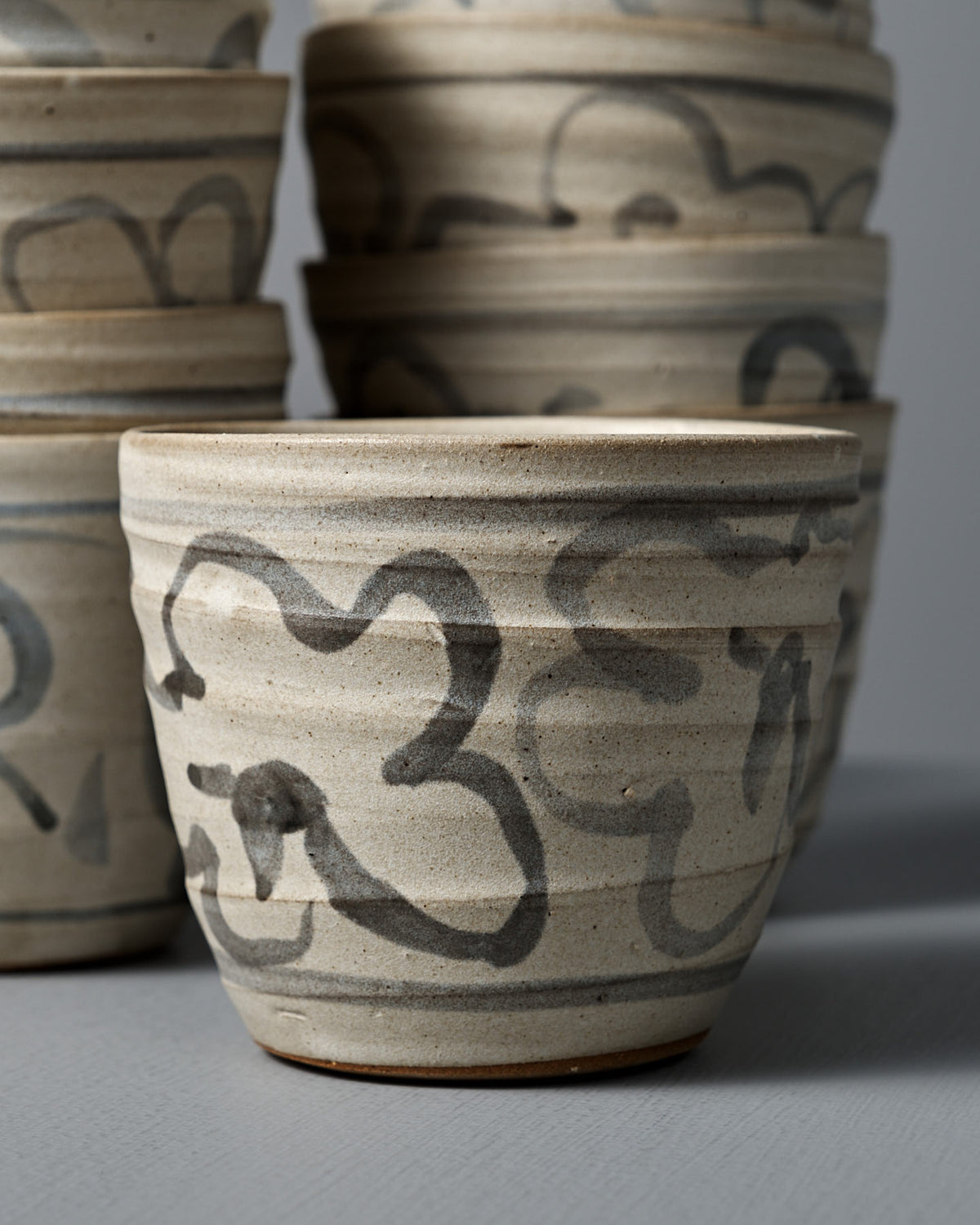 A Cup – Floral with a matte cream glaze and black abstract floral patterns is displayed atop a gray surface.