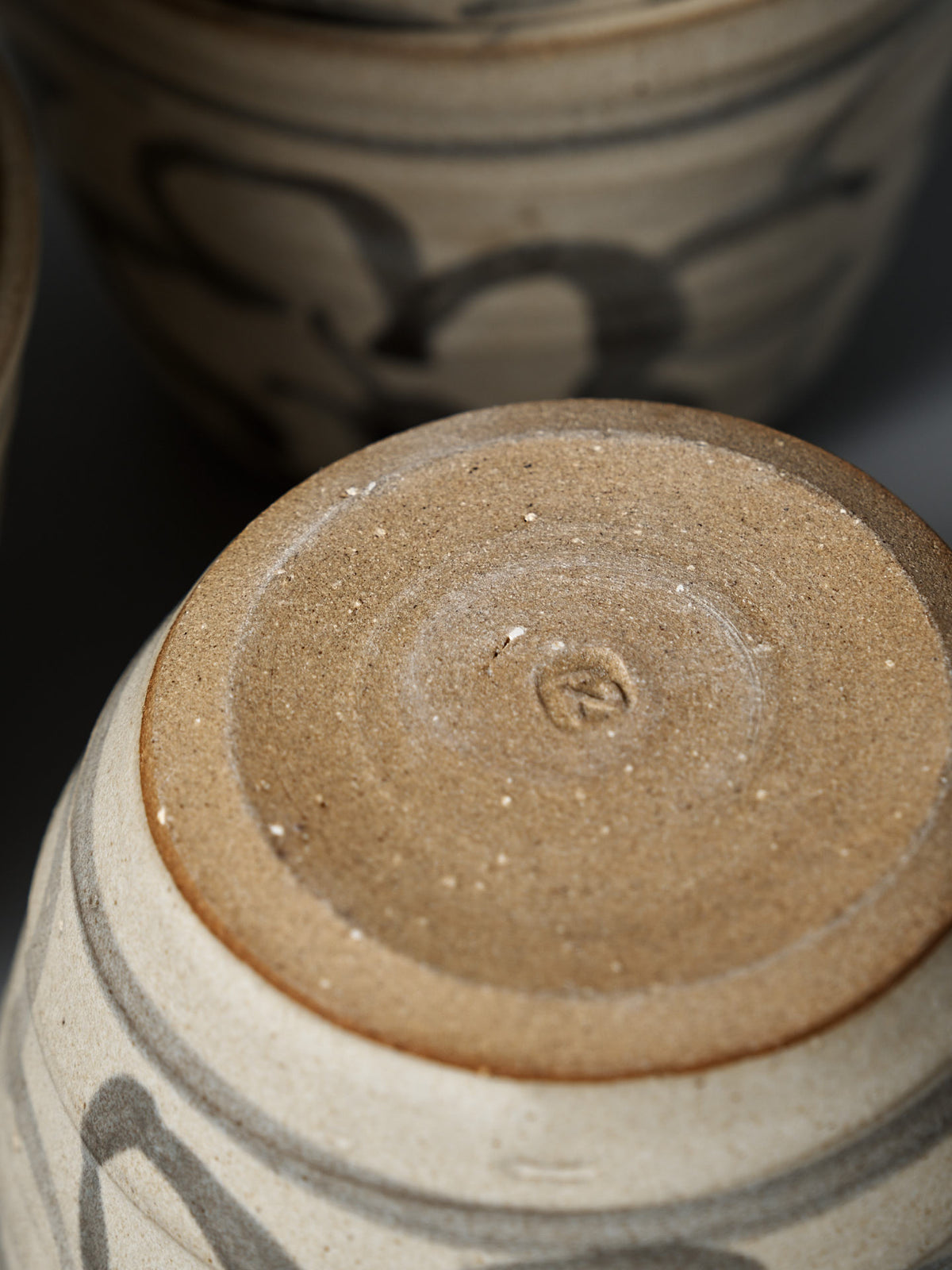 Close-up of the Cup – Floral's bottom, showing textured unglazed clay with circular markings. A matte cream glaze and subtle floral pattern are visible, with similar cups in the background.