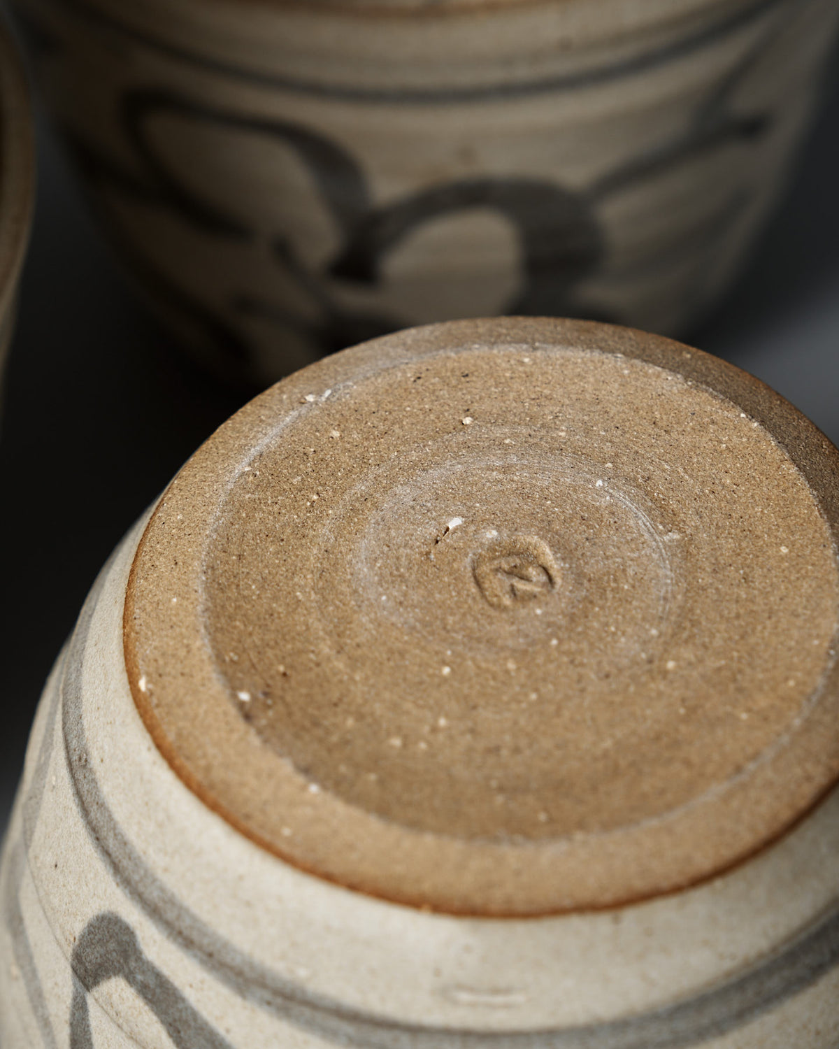 Close-up of the Cup – Floral's bottom, showing textured unglazed clay with circular markings. A matte cream glaze and subtle floral pattern are visible, with similar cups in the background.