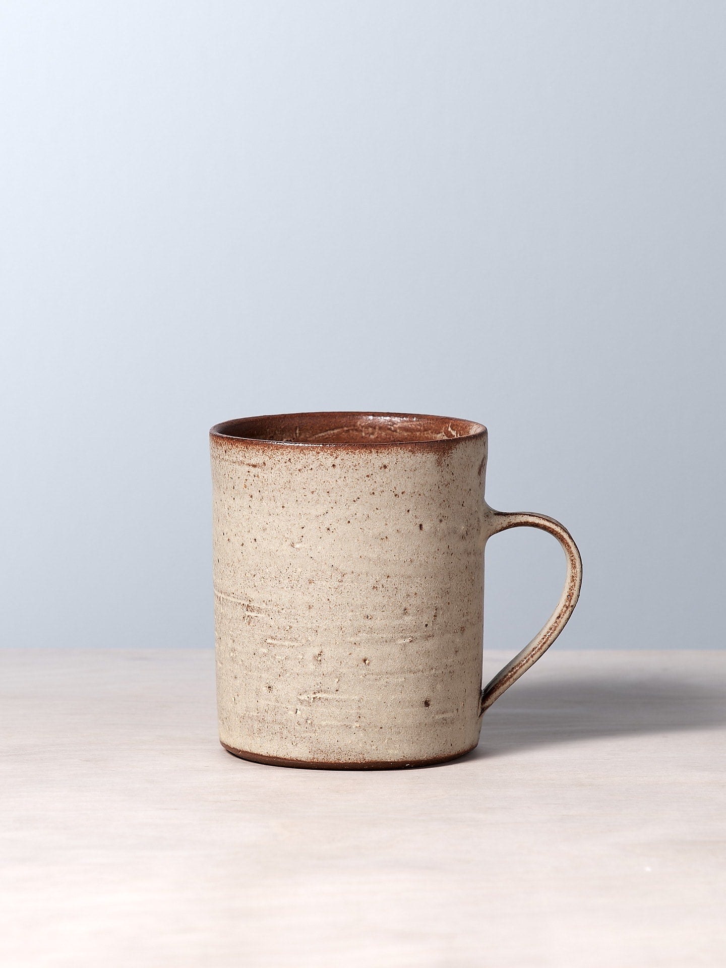 A Zoë Isaacs Mug - Cream sitting on a table with a grey background.