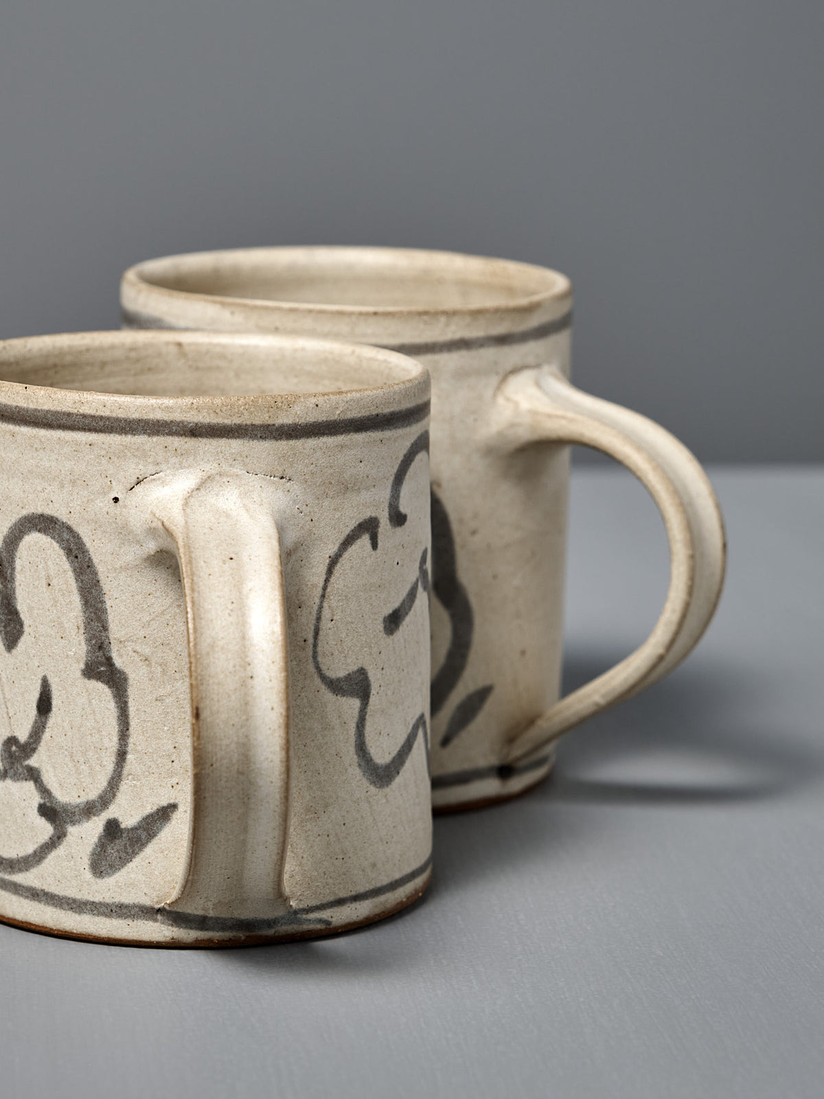 Two Mug – Floral handmade ceramic mugs featuring hand-painted abstract black designs are displayed on a gray surface with a gray background.