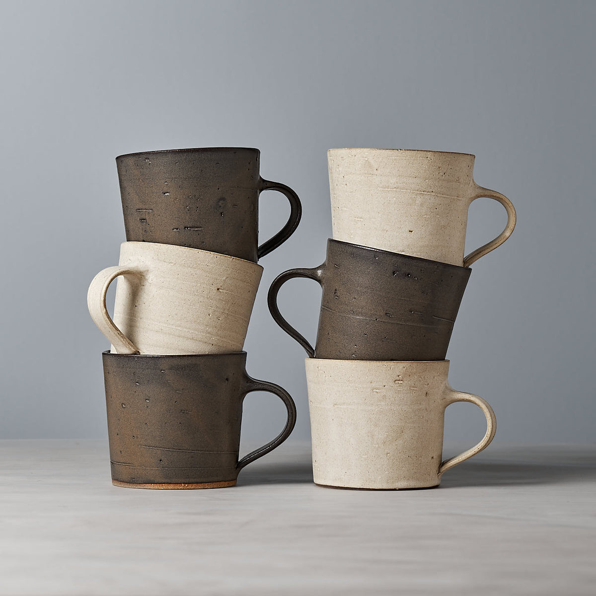 A collection of three beige and three brown ceramic mugs with a matte cream glaze, elegantly displayed on a gray background. The product is named &quot;Coffee Cup – Seafoam&quot; by Zoë Isaacs.