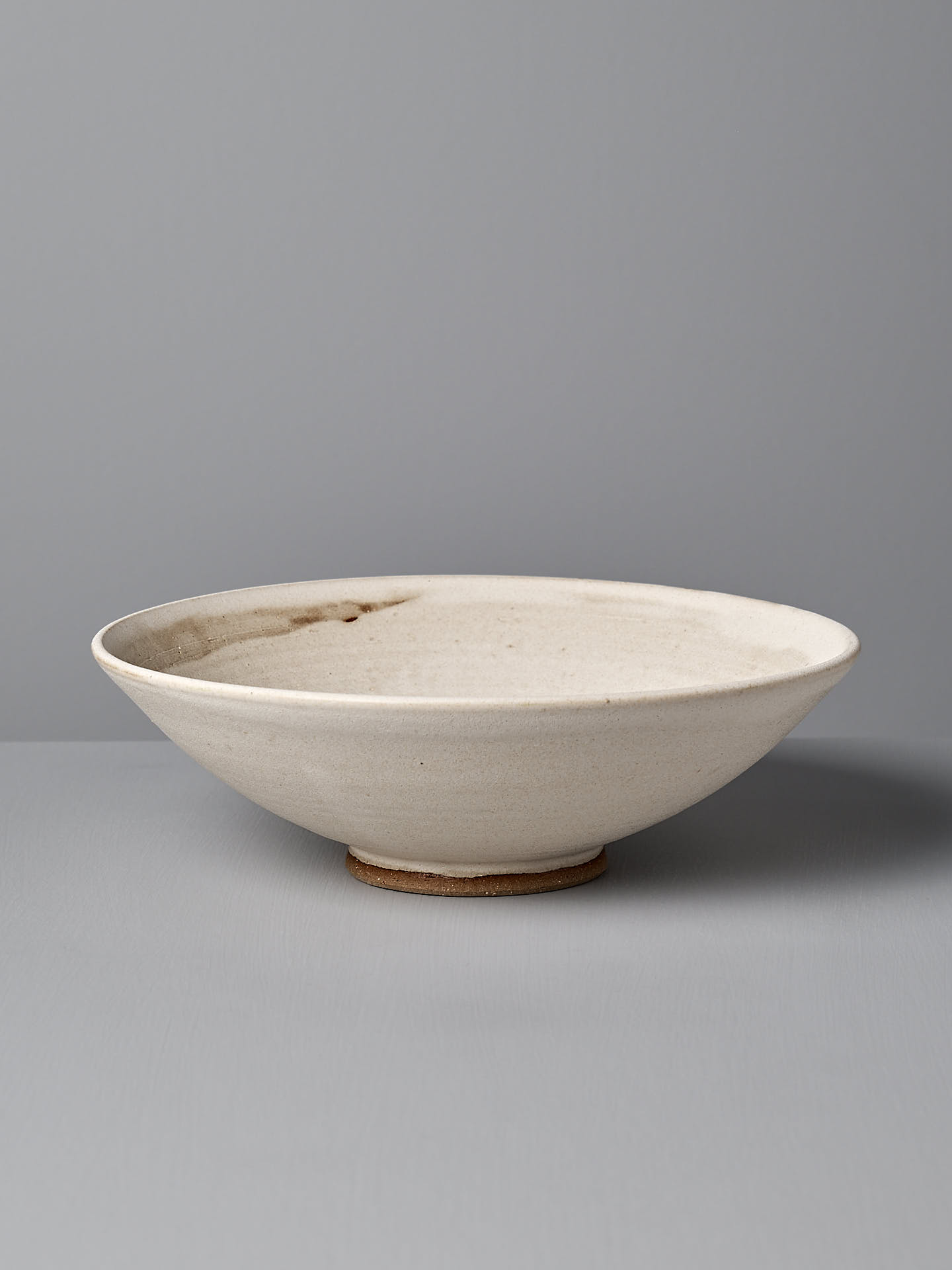 A wide, shallow ceramic serving bowl by Zoë Isaacs, made from toast-colored clay with a matte seafoam glaze and slight imperfections, sits on a flat, grey surface against a grey background.