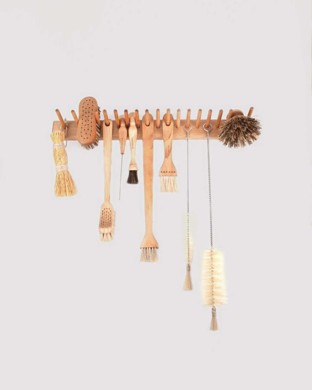 The Knopplist Hook Rack in oiled maple by Iris Hantverk beautifully showcases an assortment of kitchen brushes, such as bottle and dish brushes, set against a light backdrop.