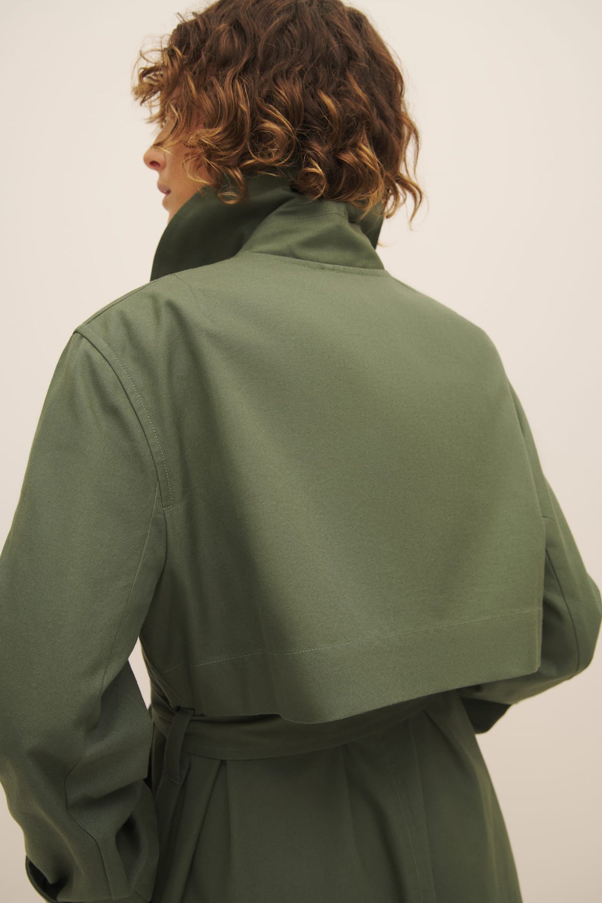 A person seen from behind wearing a Cleo Trench Coat in Sage with the collar turned up, designed for a relaxed fit by Kowtow.