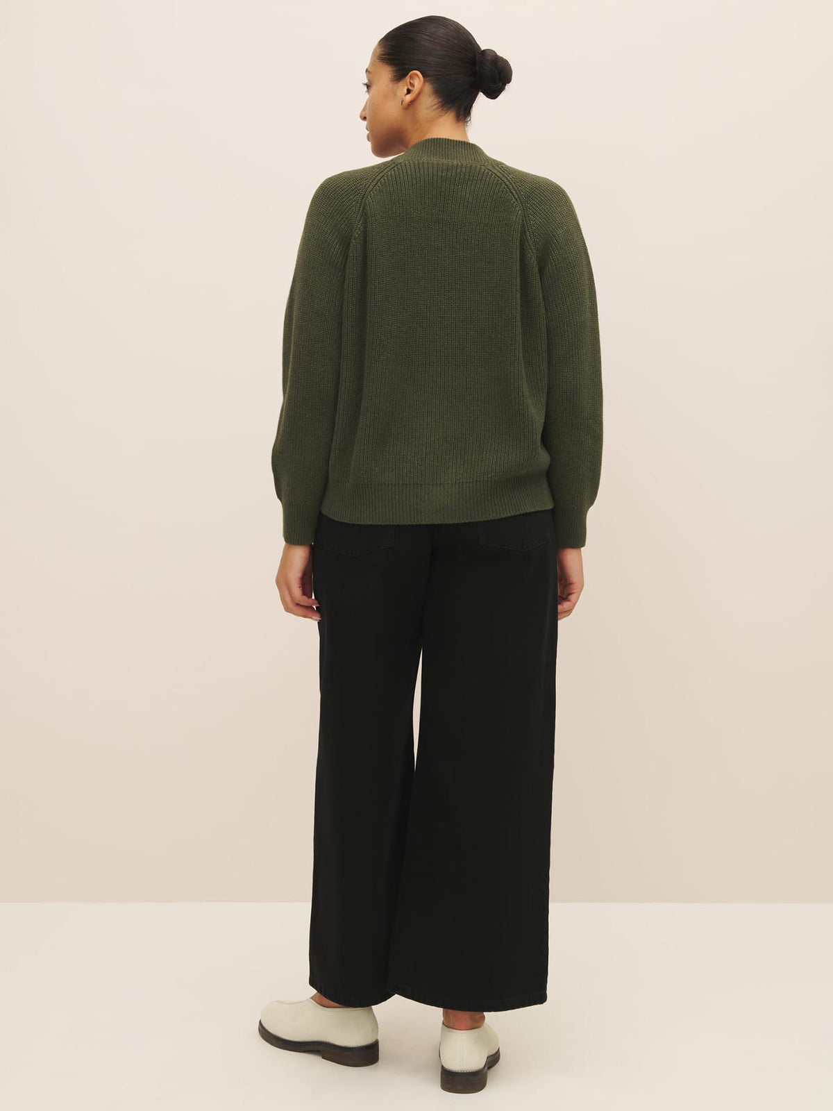 A person wearing a Hannes Cardigan in Khaki Marle from Kowtow and black pants standing with their back to the camera.