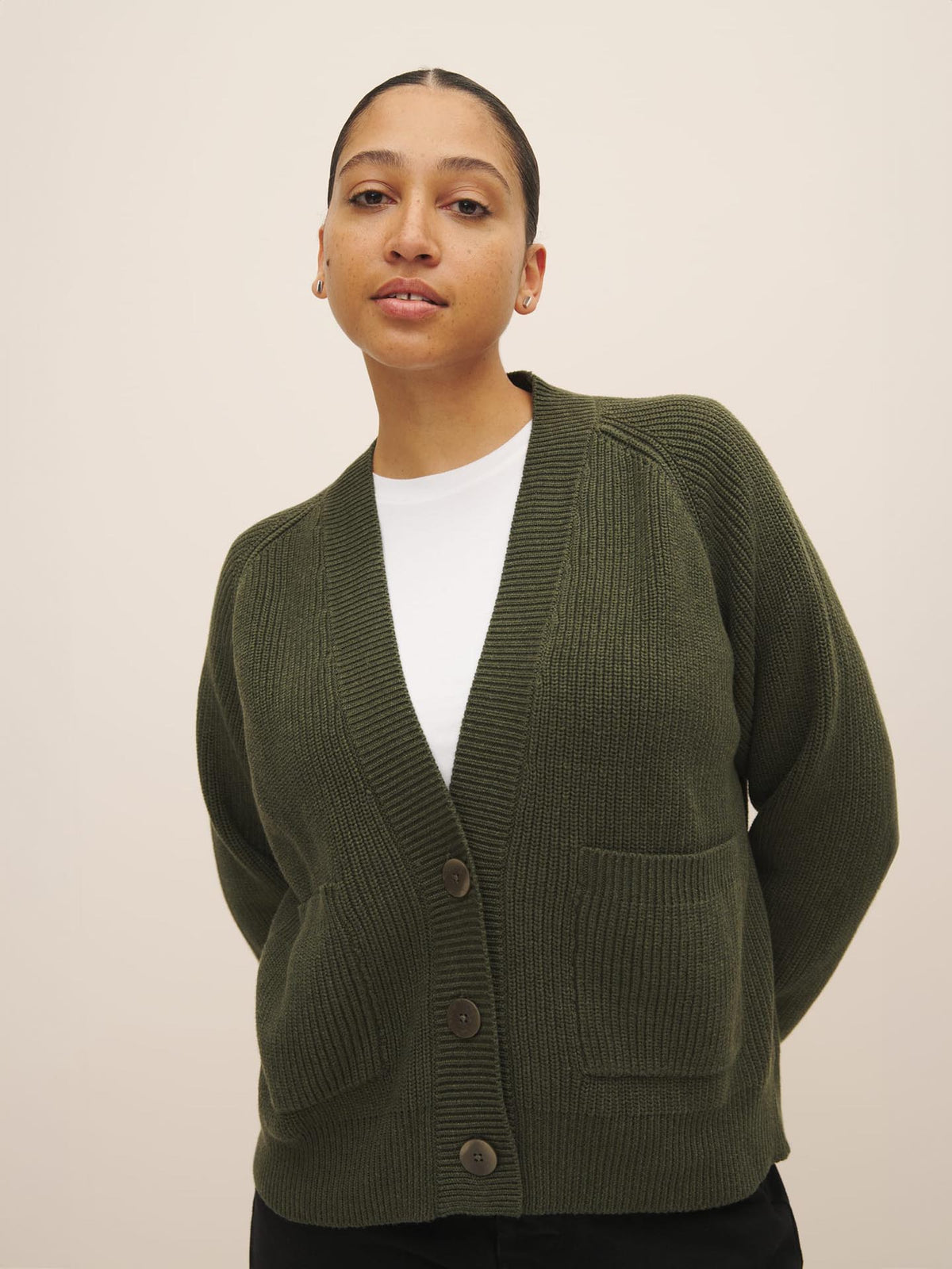 Woman in a white top and green Kowtow Hannes Cardigan – Khaki Marle standing against a neutral background.