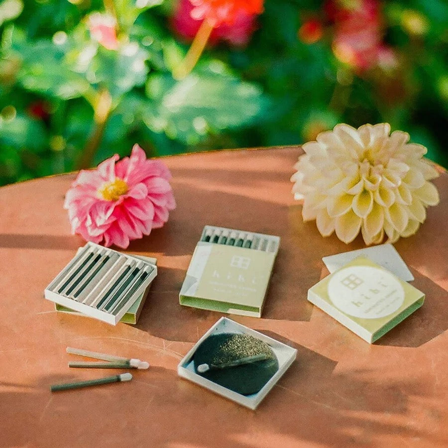 A set of hibi match box incense – garden scent gift boxes on a table next to flowers.