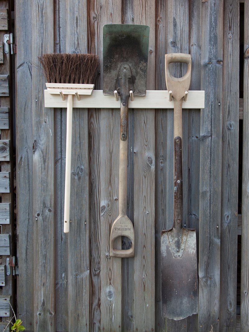 The Iris Hantverk Birchwood Garden Tool Hanger elegantly showcases a broom and two shovels outdoors.