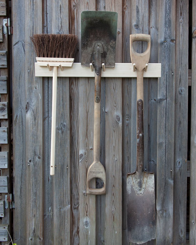 The Iris Hantverk Birchwood Garden Tool Hanger elegantly showcases a broom and two shovels outdoors.