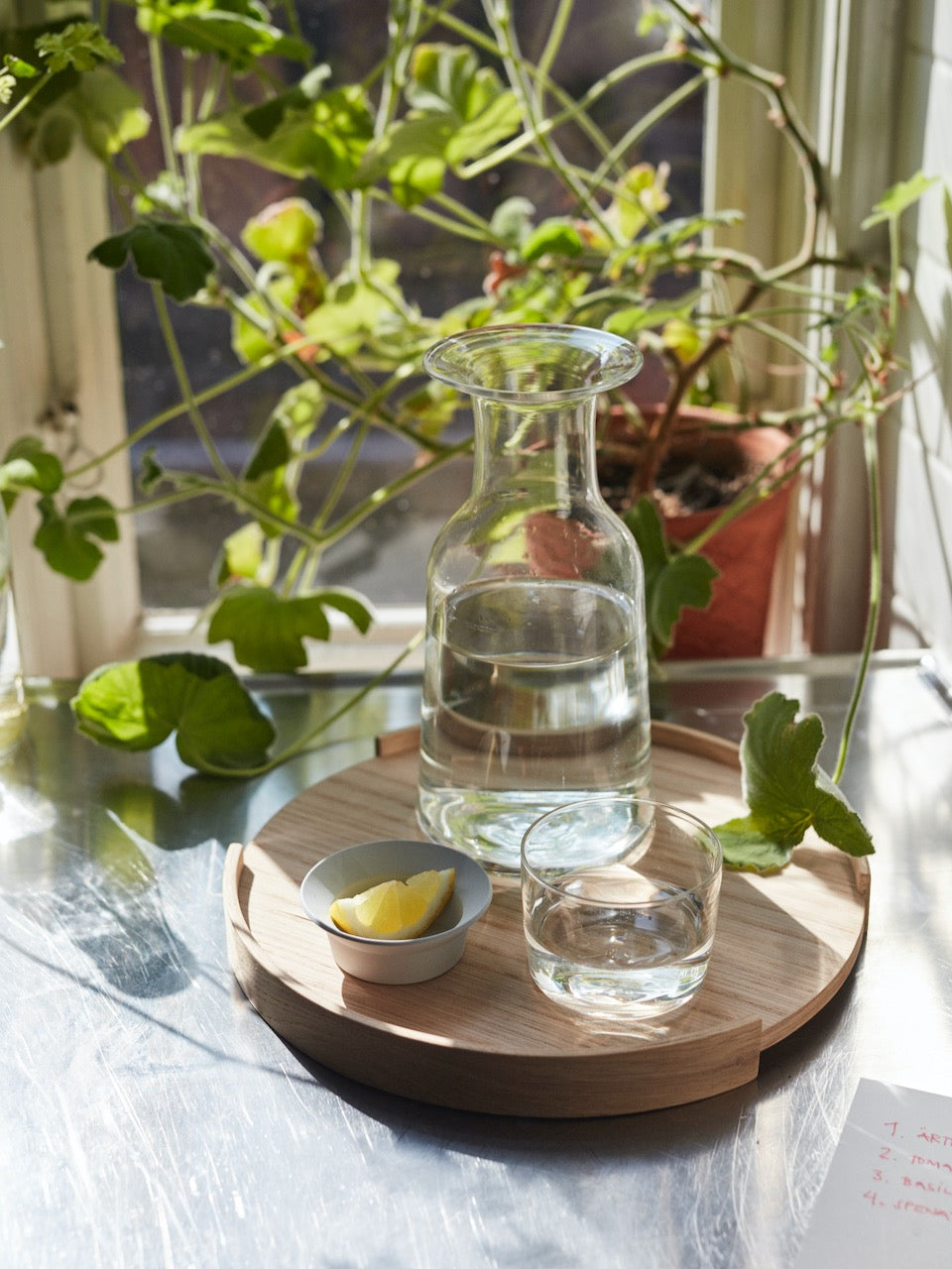 A Hammer Decanter by Skagerak on a wooden tray next to a window.