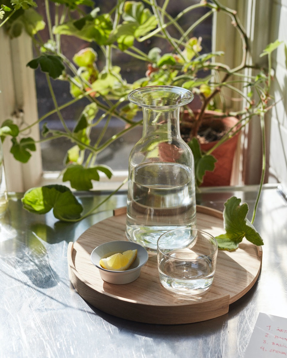 A Hammer Decanter by Skagerak on a wooden tray next to a window.
