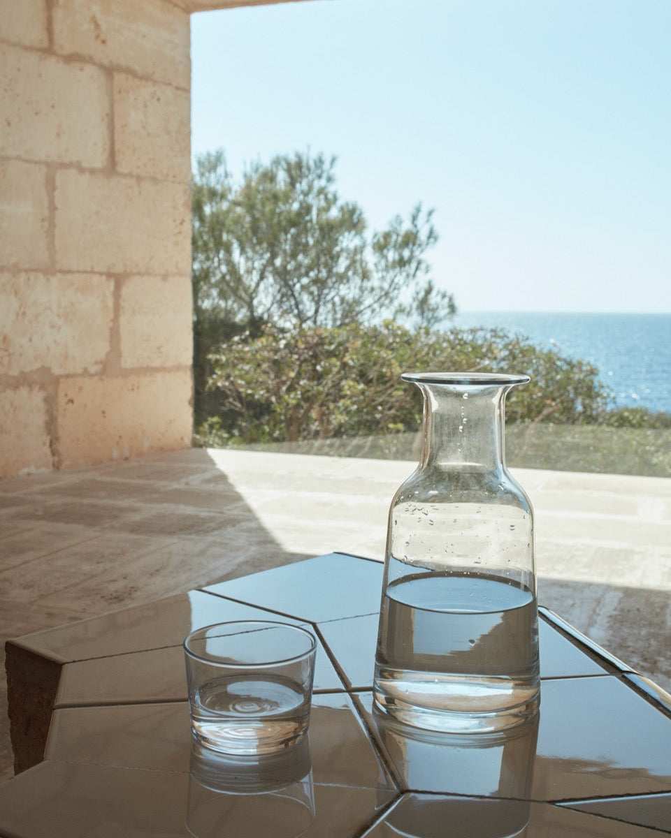 A Skagerak Hammer Decanter and a glass of water on a table.
