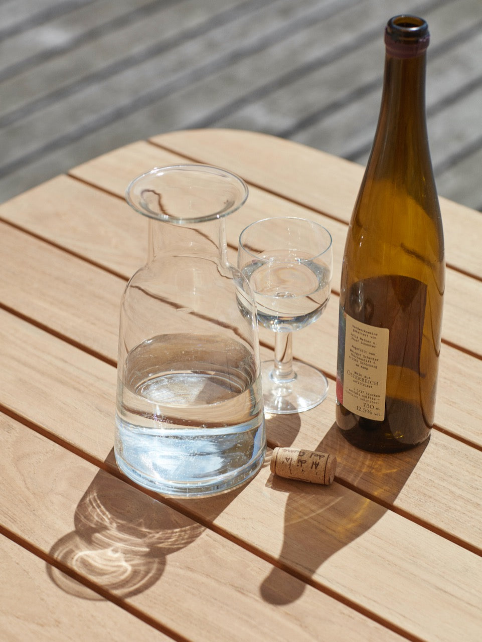 A Hammer Decanter by Skagerak and a glass of water on a wooden table.