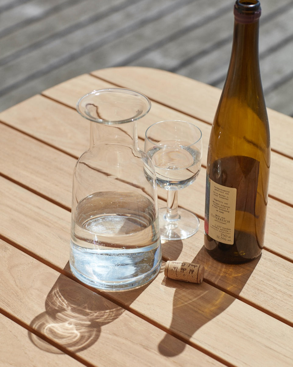 A Hammer Decanter by Skagerak and a glass of water on a wooden table.