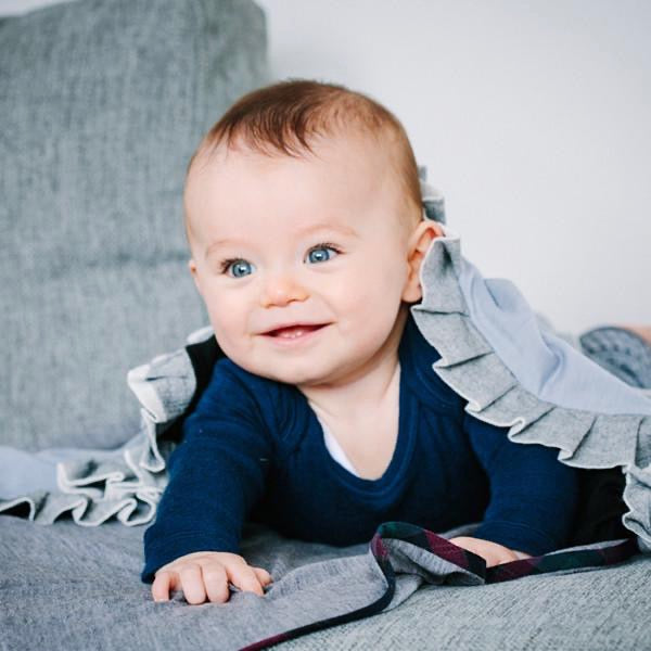 A baby wrapped in a cozy AAA Design New Zealand ZQ merino wool Baby Merino Blanket - Black/Ice Blue, resting comfortably on a couch.