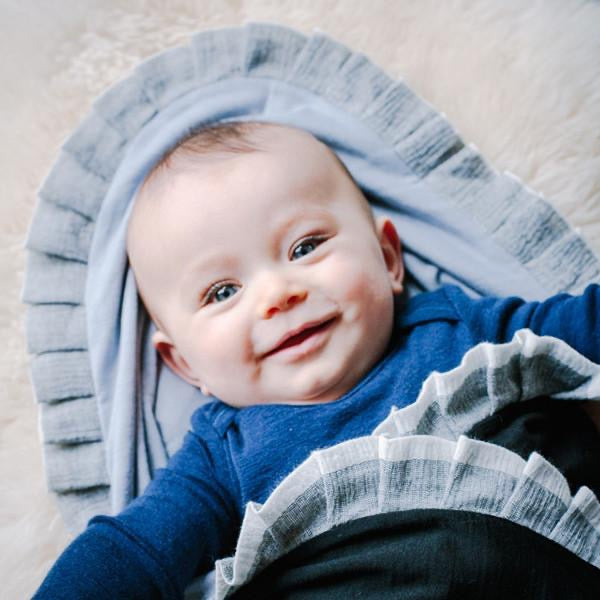 A baby nestled on a Baby Merino Blanket - Black/Ice Blue, made from New Zealand ZQ merino wool – a luxurious natural fiber by AAA Design.