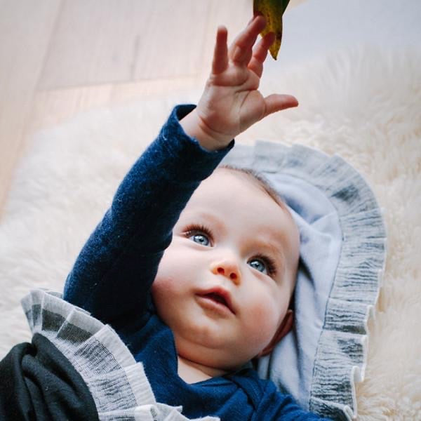 A baby lying on a white carpet with a bird in the air, wrapped in an AAA Design Baby Merino Blanket - Black/Ice Blue made from New Zealand ZQ merino wool.