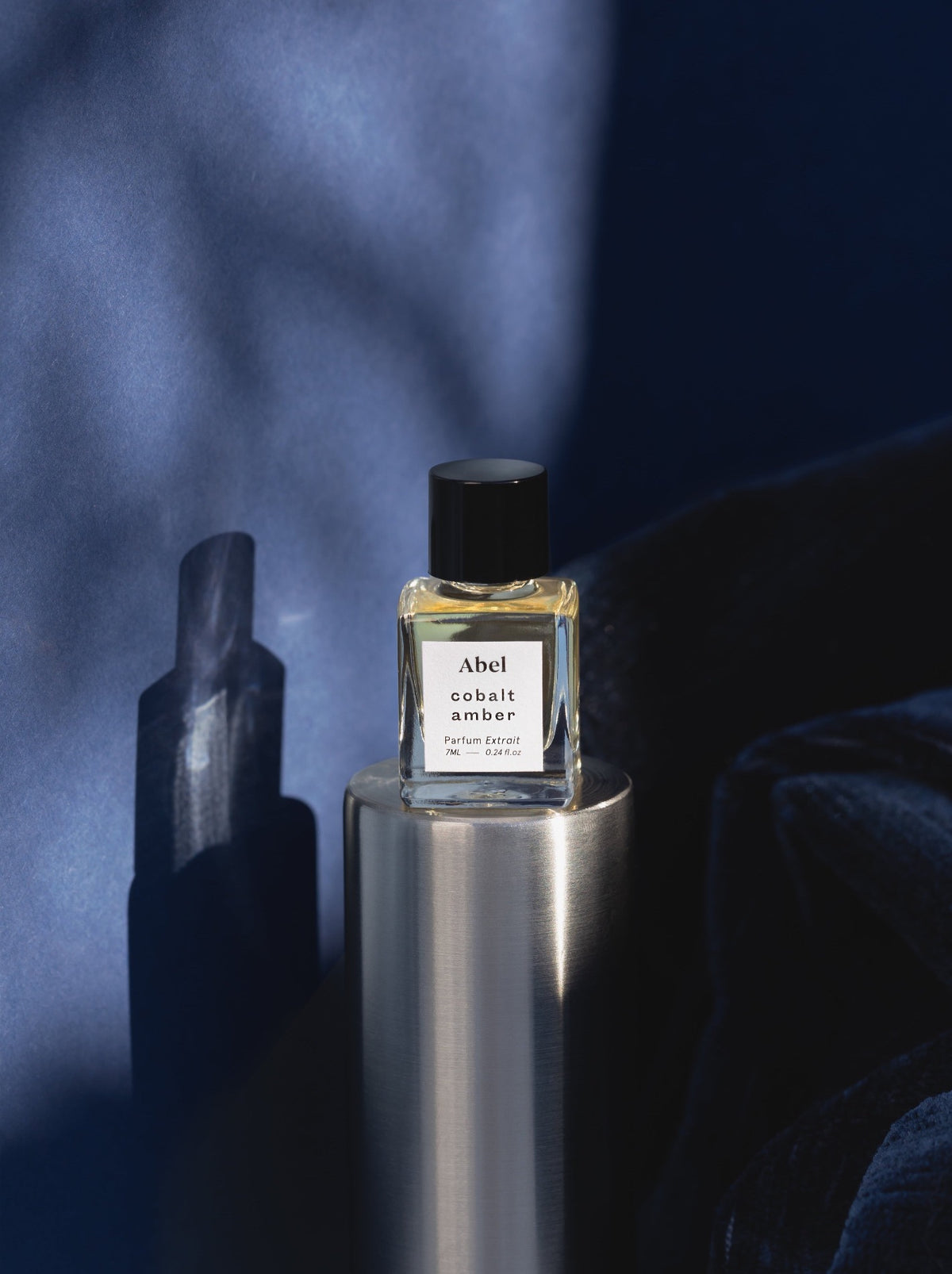 A Cobalt Amber Parfum Extrait by Abel, for comfort, sitting next to a blue background.