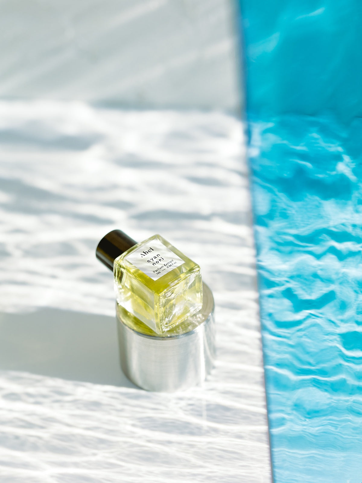 A bottle of Cyan Nori Parfum Extrait – for joy by Abel, creating a natural parfum, sitting on a table next to a pool.