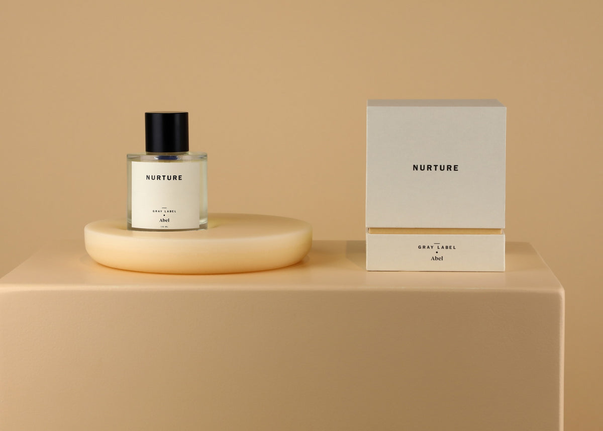 A bottle of NURTURE - grey label perfume by Abel on a table next to a box.