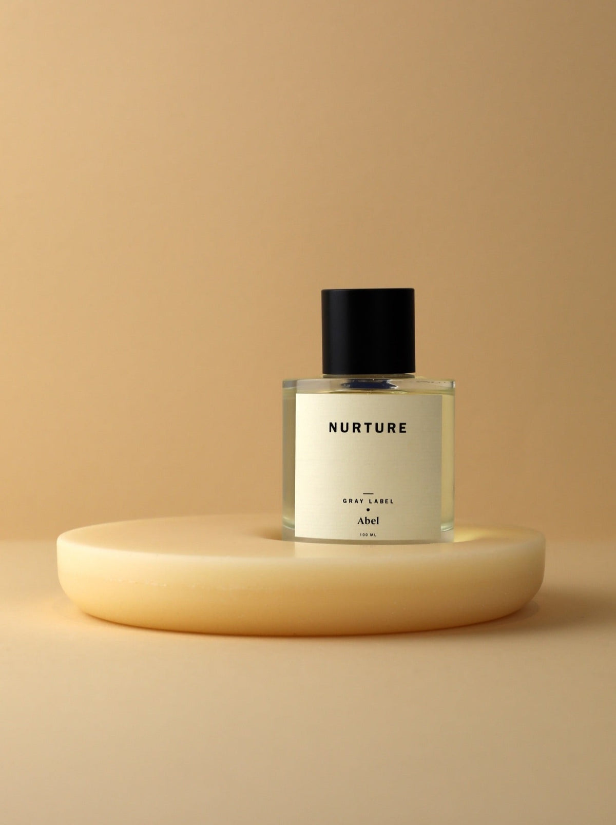 A bottle of NURTURE - grey label perfume sitting on top of a yellow plate, promoting fairtrade and sustainable farming practices. (Brand: Abel)