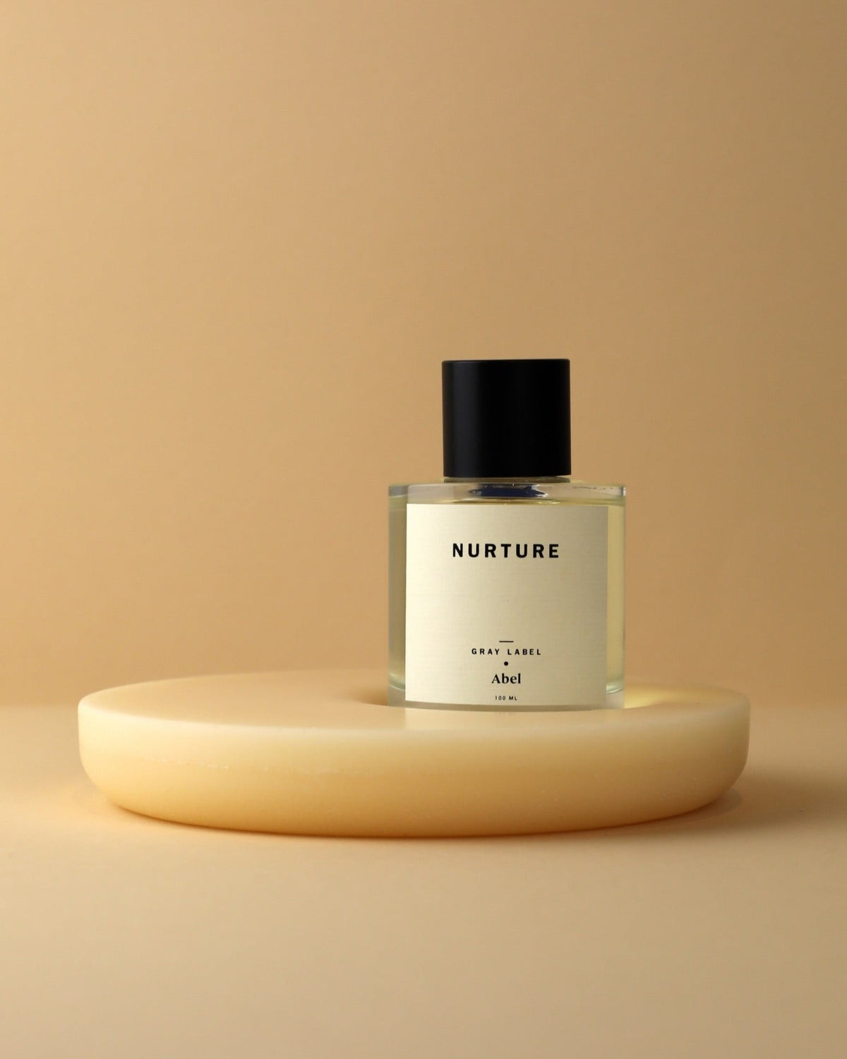 A bottle of NURTURE - grey label perfume sitting on top of a yellow plate, promoting fairtrade and sustainable farming practices. (Brand: Abel)