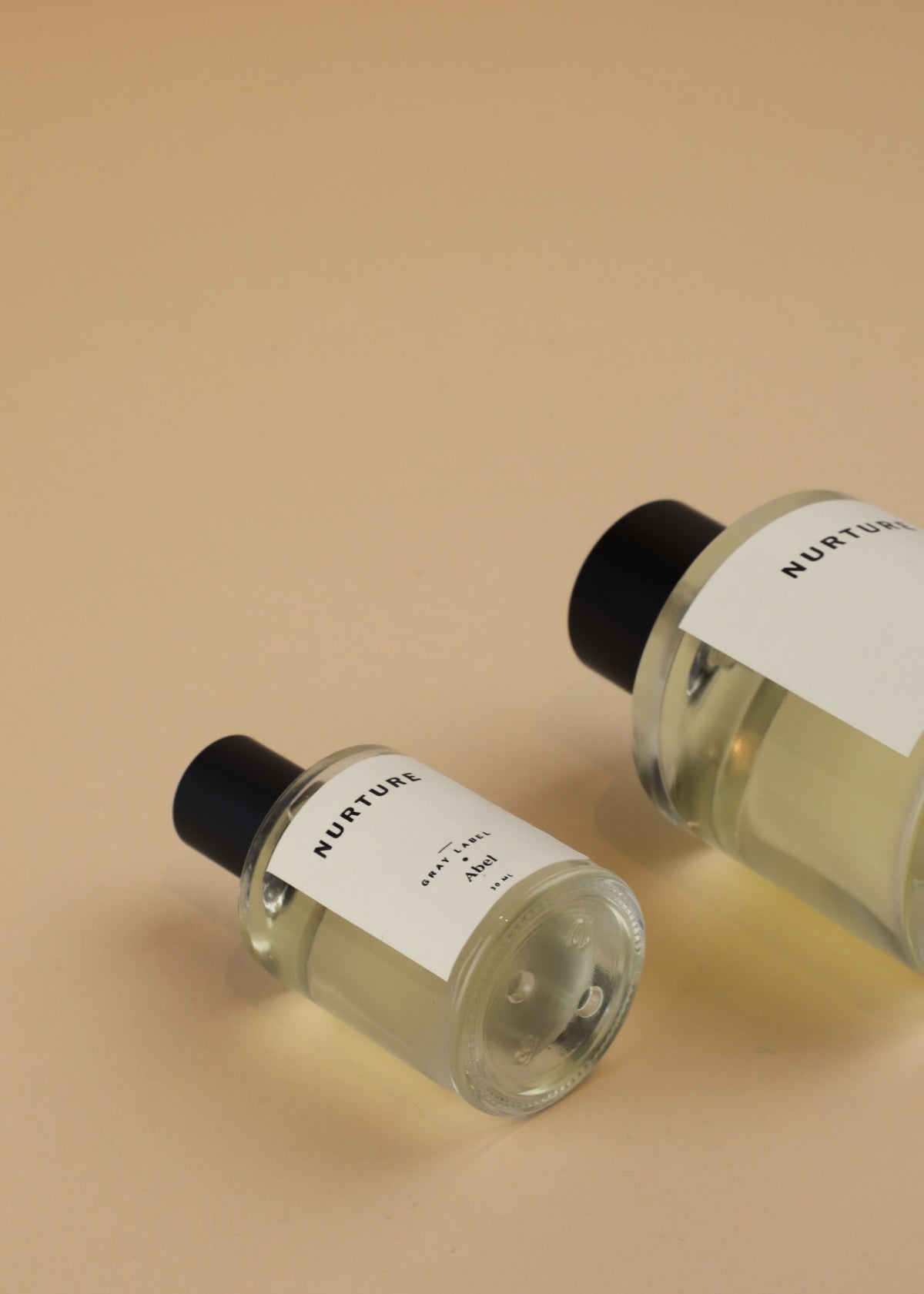 Two bottles of NURTURE - grey label sandalwood perfume on a beige surface. Brand: Abel.