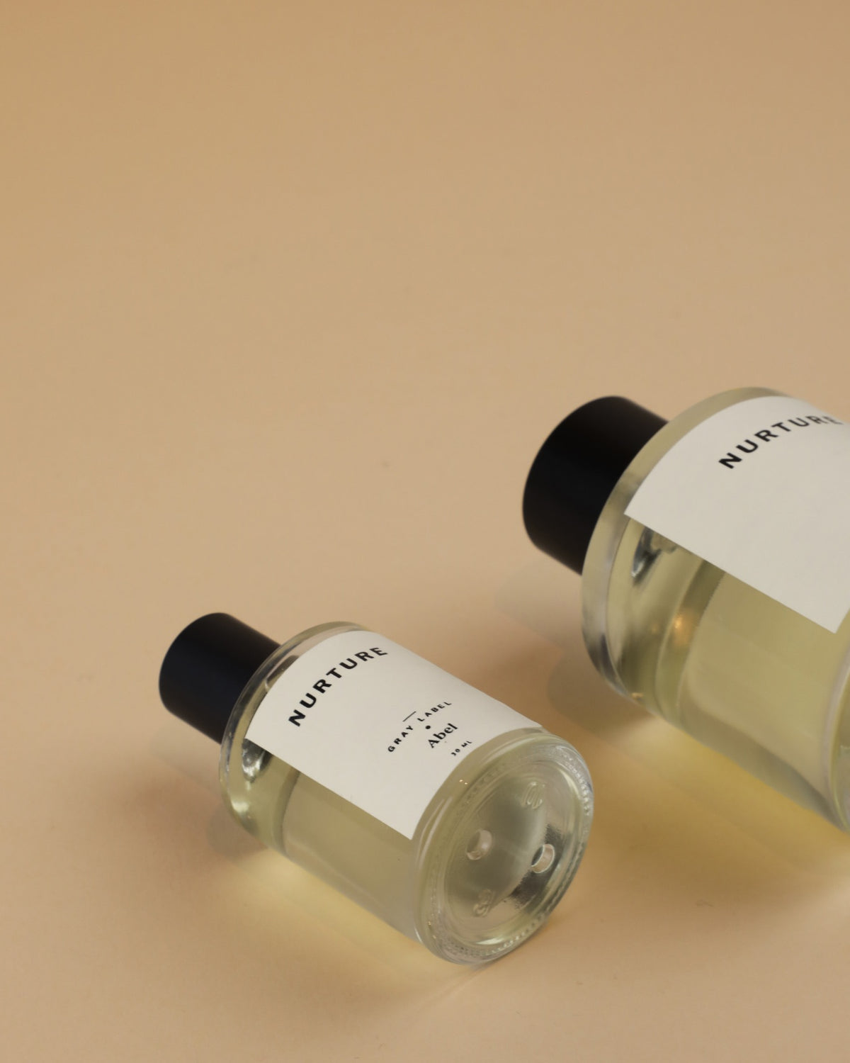 Two bottles of NURTURE - grey label sandalwood perfume on a beige surface. Brand: Abel.