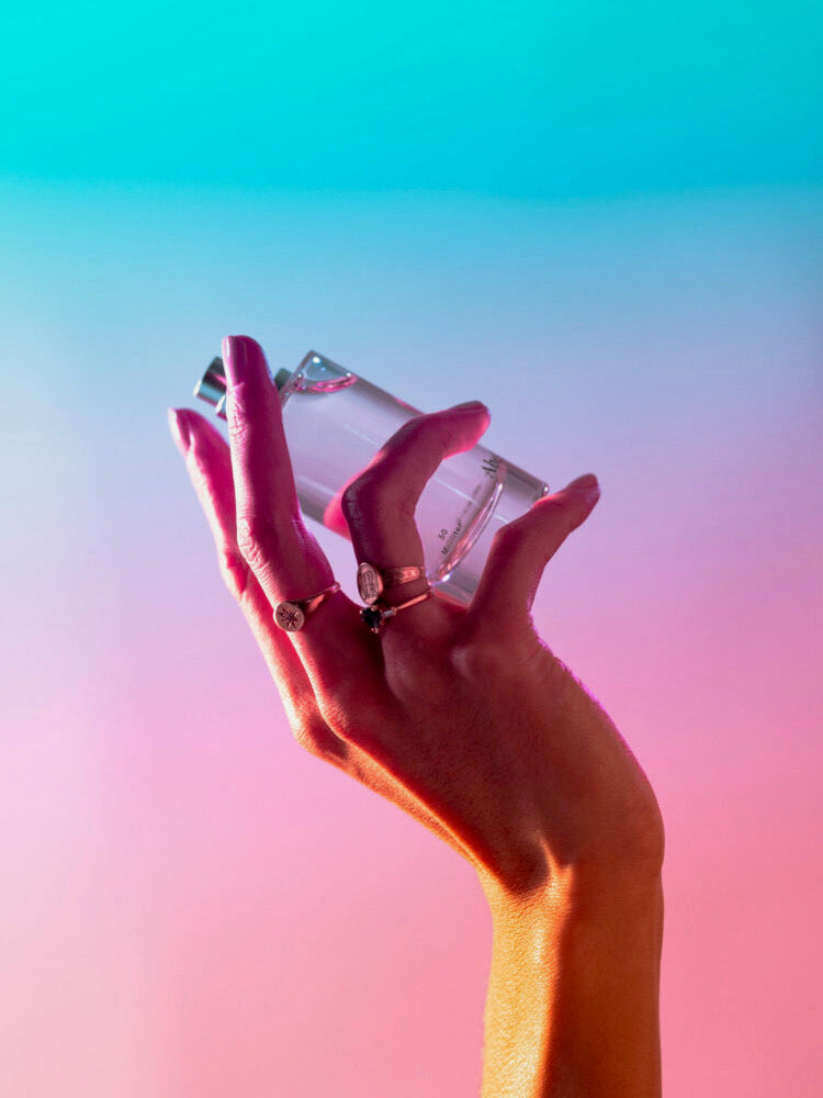 A woman holding a bottle of Cyan Nori – a sweet, salty musk perfume by Abel in front of a colorful background that blurs the line between salty deep-sea and sustainable farming practices.
