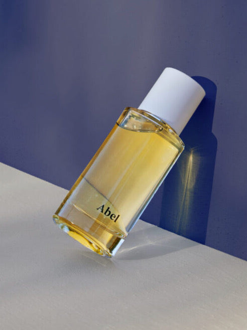 A bottle of Abel perfume, Cobalt Amber – a chic, sultry oriental, on a blue surface, featuring 100% natural eau de parfum crafted with sustainable farming practices.