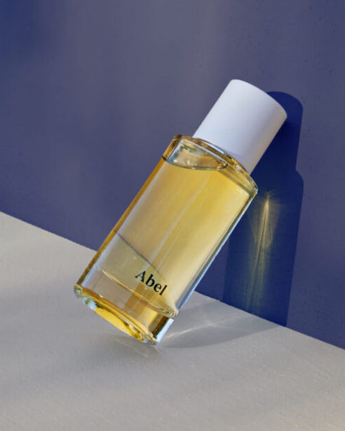 A bottle of Abel perfume, Cobalt Amber – a chic, sultry oriental, on a blue surface, featuring 100% natural eau de parfum crafted with sustainable farming practices.